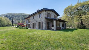 A stone house with a porch, surrounded by a grassy lawn and trees. - Villa 'Agriturismo Casa Del Castagneto' with Lake View, Private Terrace & Wi-Fi (Gargnano)