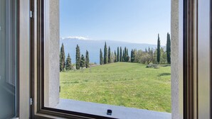 A window view of a grassy field with trees and a distant mountain range. - Villa 'Agriturismo Casa Del Castagneto' with Lake View, Private Terrace & Wi-Fi (Gargnano)