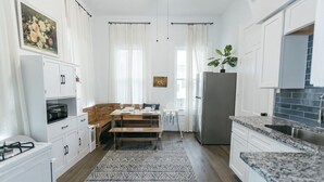 A modern kitchen with white cabinetry, a dining area with a wooden table, and a patterned rug.