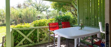 A covered outdoor patio with a table and chairs, surrounded by greenery.