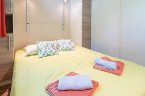 Una cama bien hecha con almohadas, una colcha amarilla y dos toallas dobladas sobre la cama.