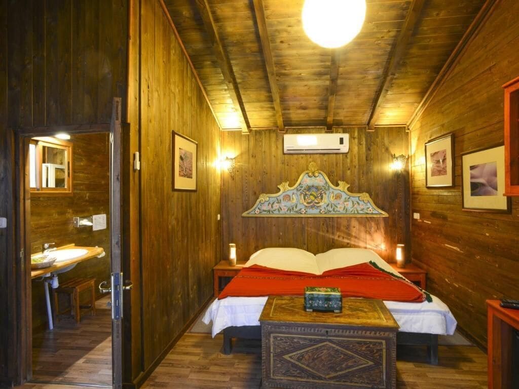Una habitación de madera con una cama, una mesita pequeña y un aire acondicionado instalado en la pared.