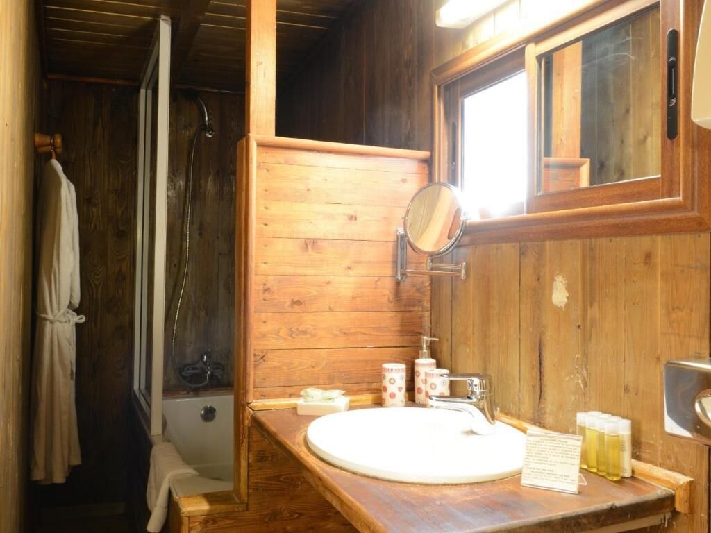 Een houten badkamertje in een chalet, met een bad, een wastafel en een spiegel.