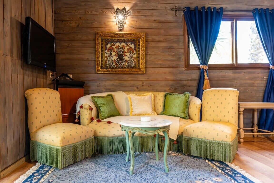 A cozy room with a wooden wall, a sofa with green and yellow cushions, a small table, and a TV mounted on the wall.