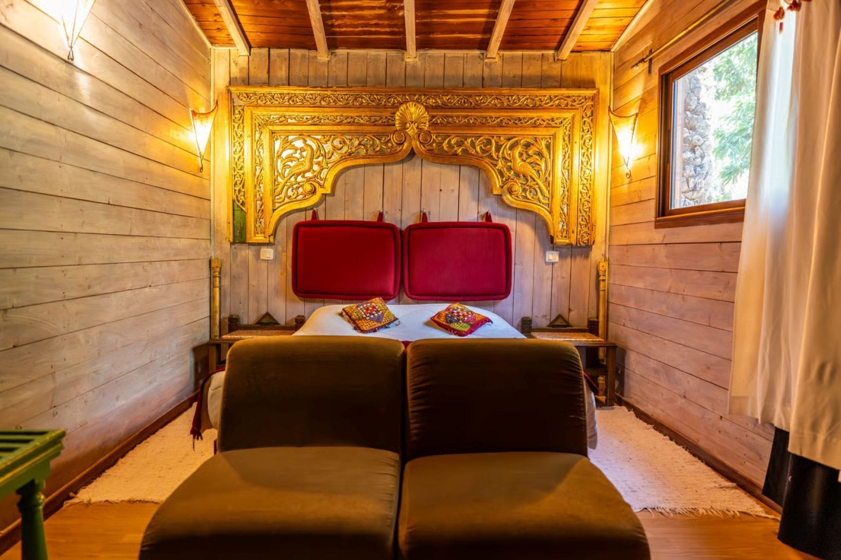 Camera da letto in una baita di legno, con un letto grande, due testiere rosse e una testiera decorata con intagli.