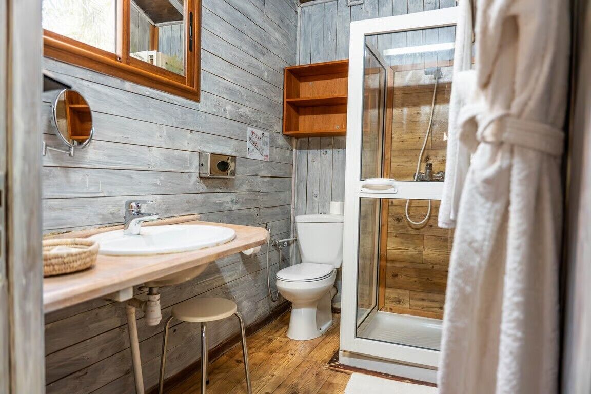 A bathroom with a wooden wall, a white sink, a toilet, and a glass shower enclosure.
