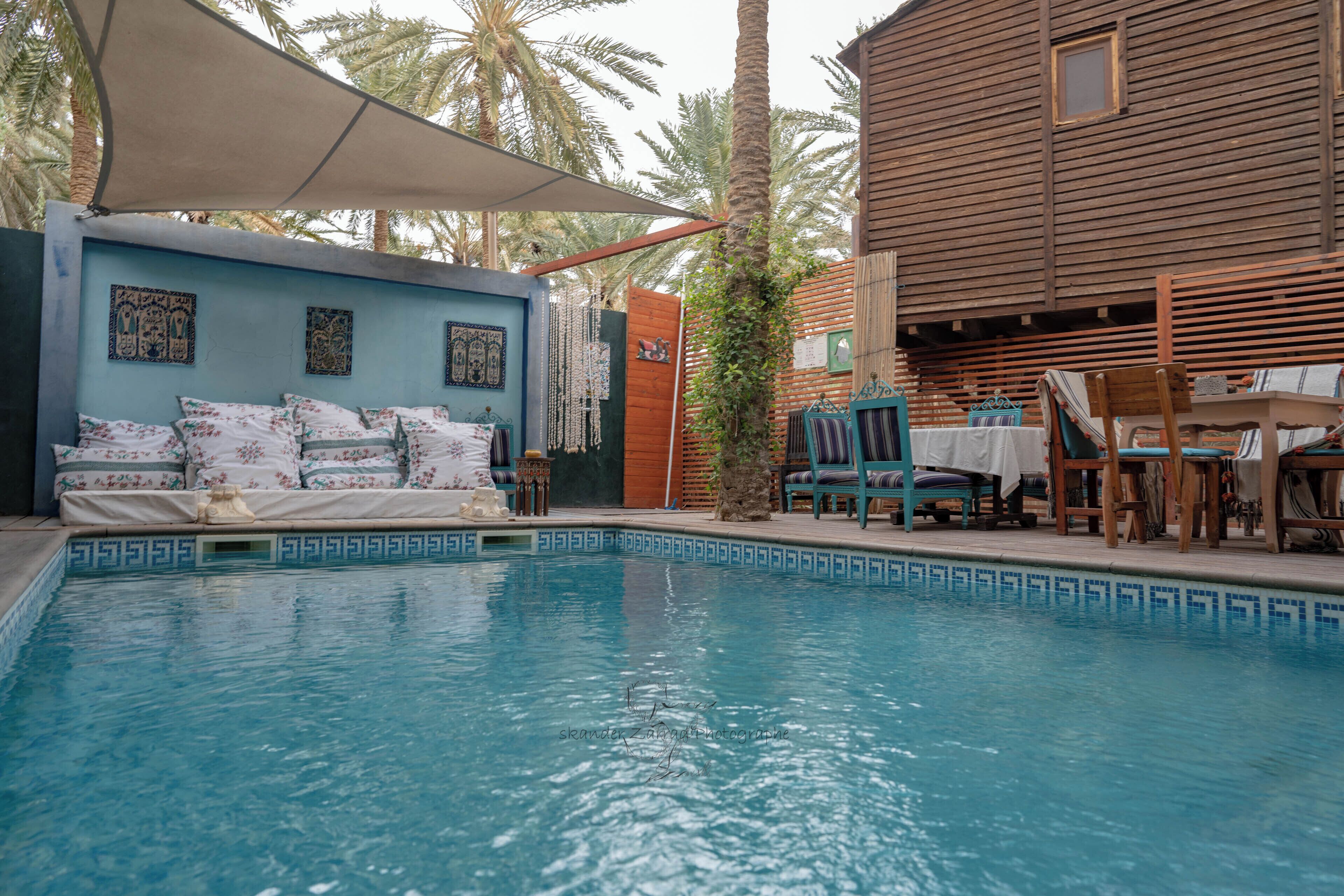 A pool area with a blue wall, a wooden building, and a covered seating area.