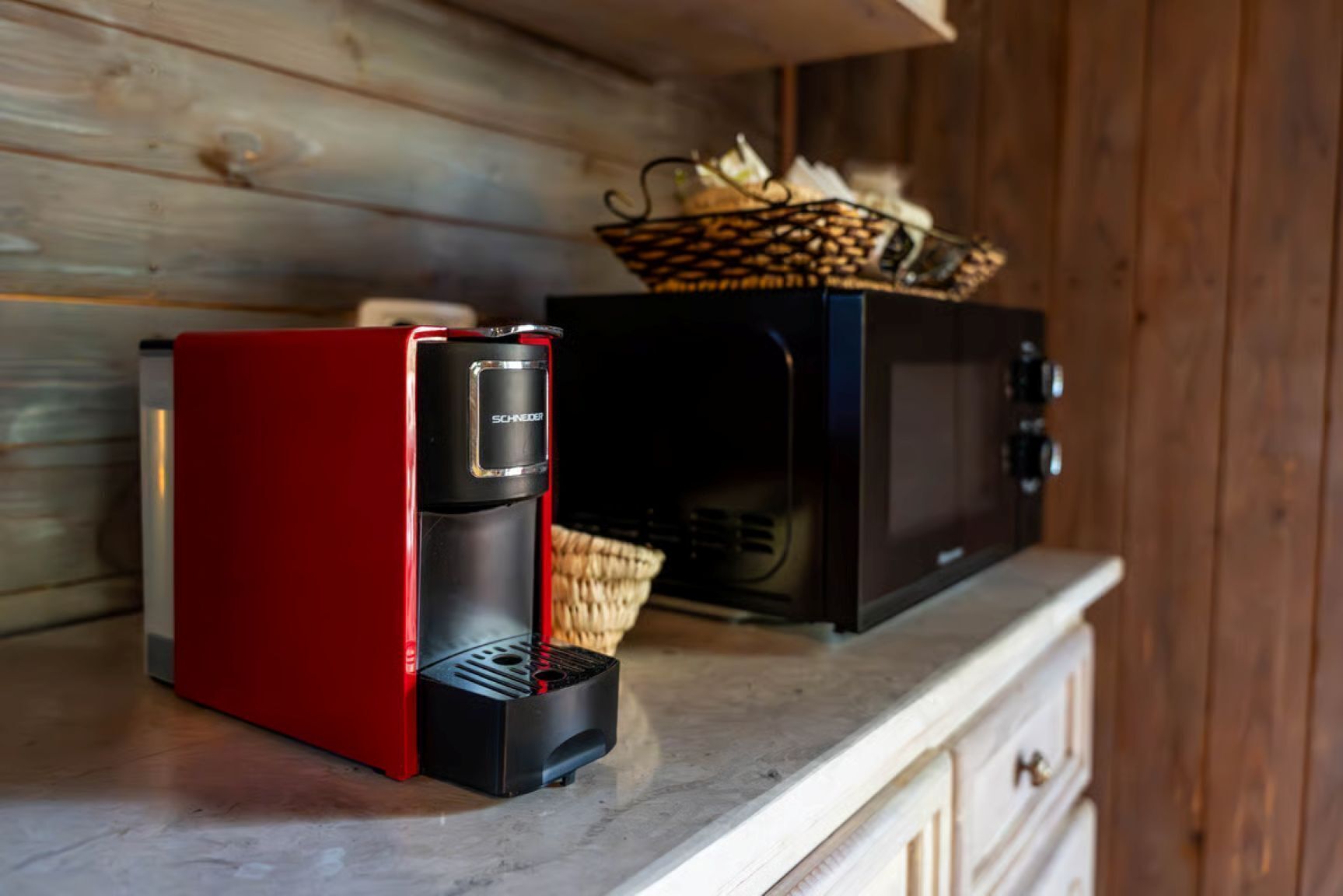A red coffee maker and a black microwave on a wooden countertop.