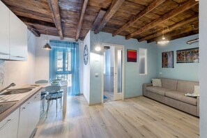 A modern kitchen with wooden beams, a dining area with chairs, a sofa, and artwork on the walls. - Prima del cielo – Lake Apartment (Esino Lario)