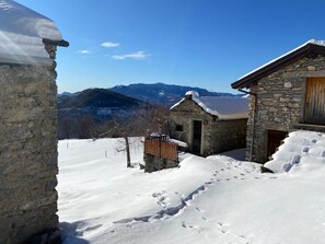 Un edificio de piedra con puerta de madera, rodeado de nieve y montañas al fondo.