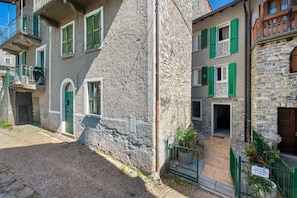 A stone building with green shutters, a cobblestone street, and a small garden area.