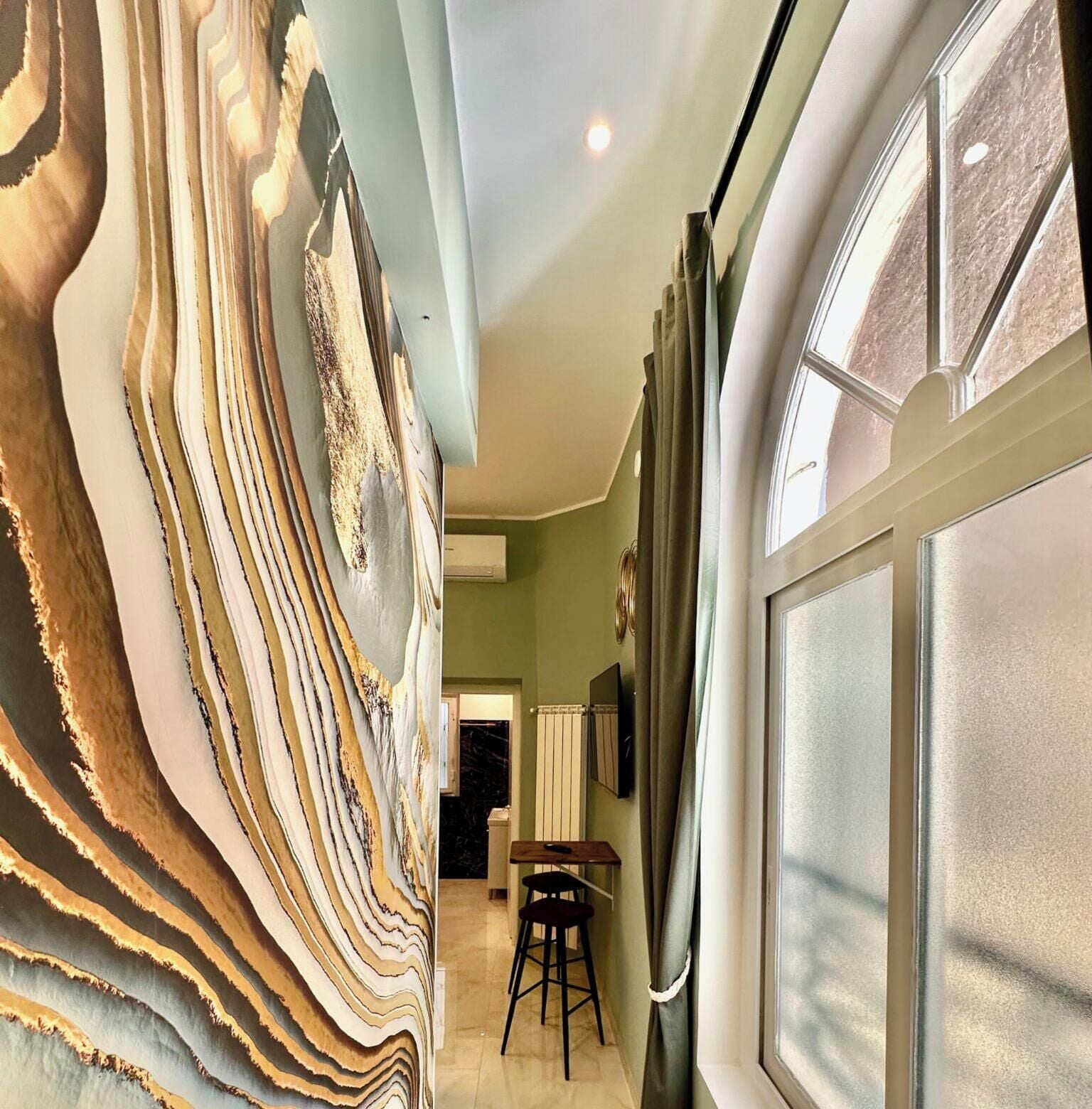 Une pièce avec un grand tableau abstrait au mur, une fenêtre avec des rideaux et une petite table avec une chaise.