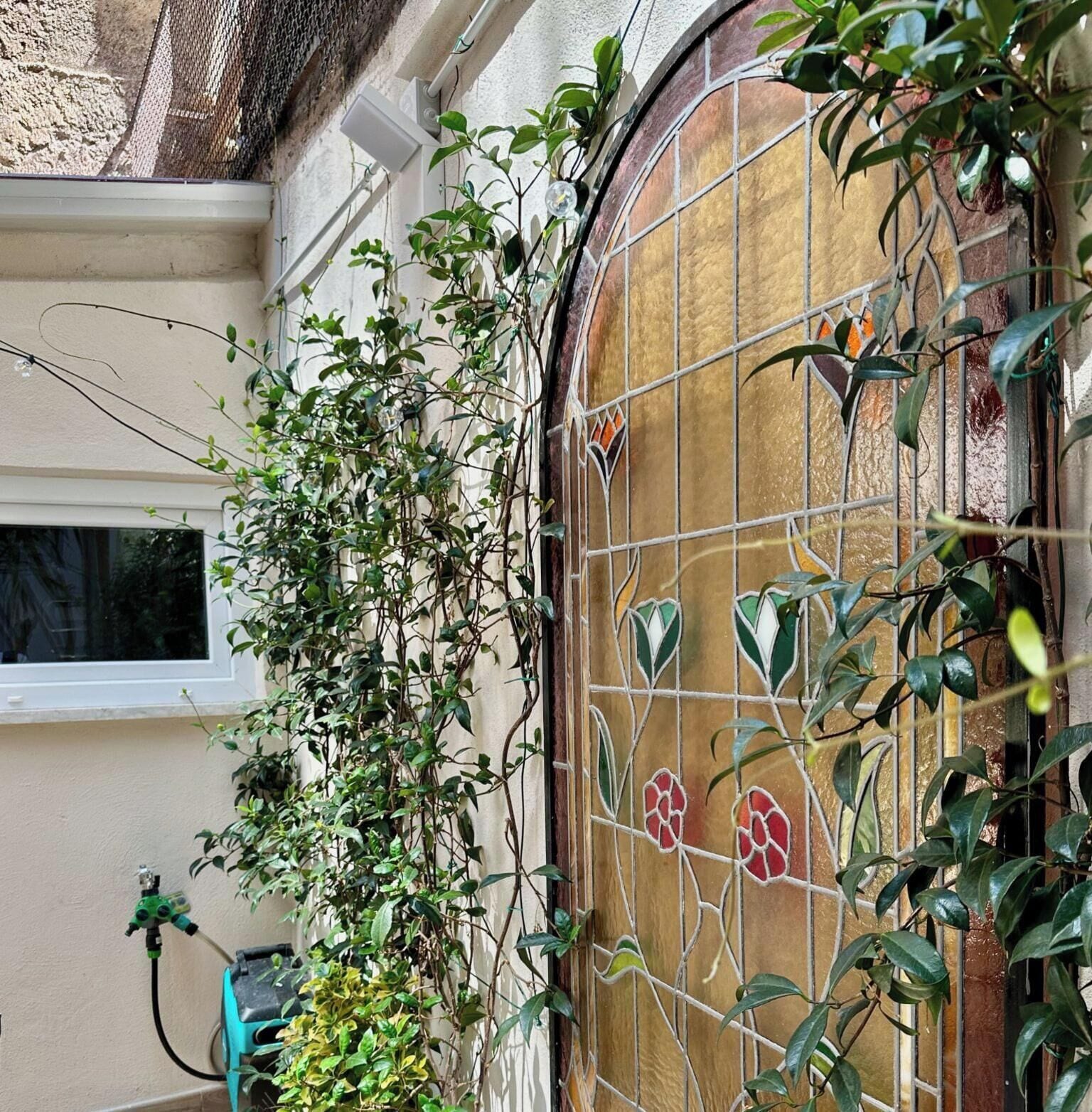 A window with a decorative stained glass design, a white window frame, and a wall with a textured surface.