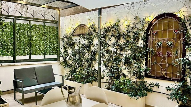 A modern interior with a seating area, a decorative wall with climbing plants, and a stained glass window. - Vacanze Romane Suite 7 Languages (Rome)