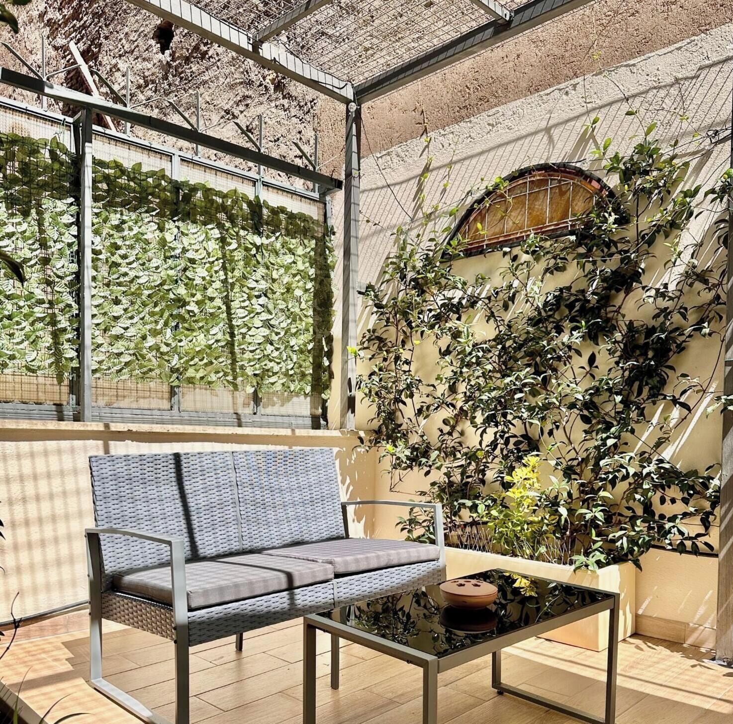 A modern interior with a glass ceiling, a cushioned bench, a glass table, and a wall covered in climbing plants.