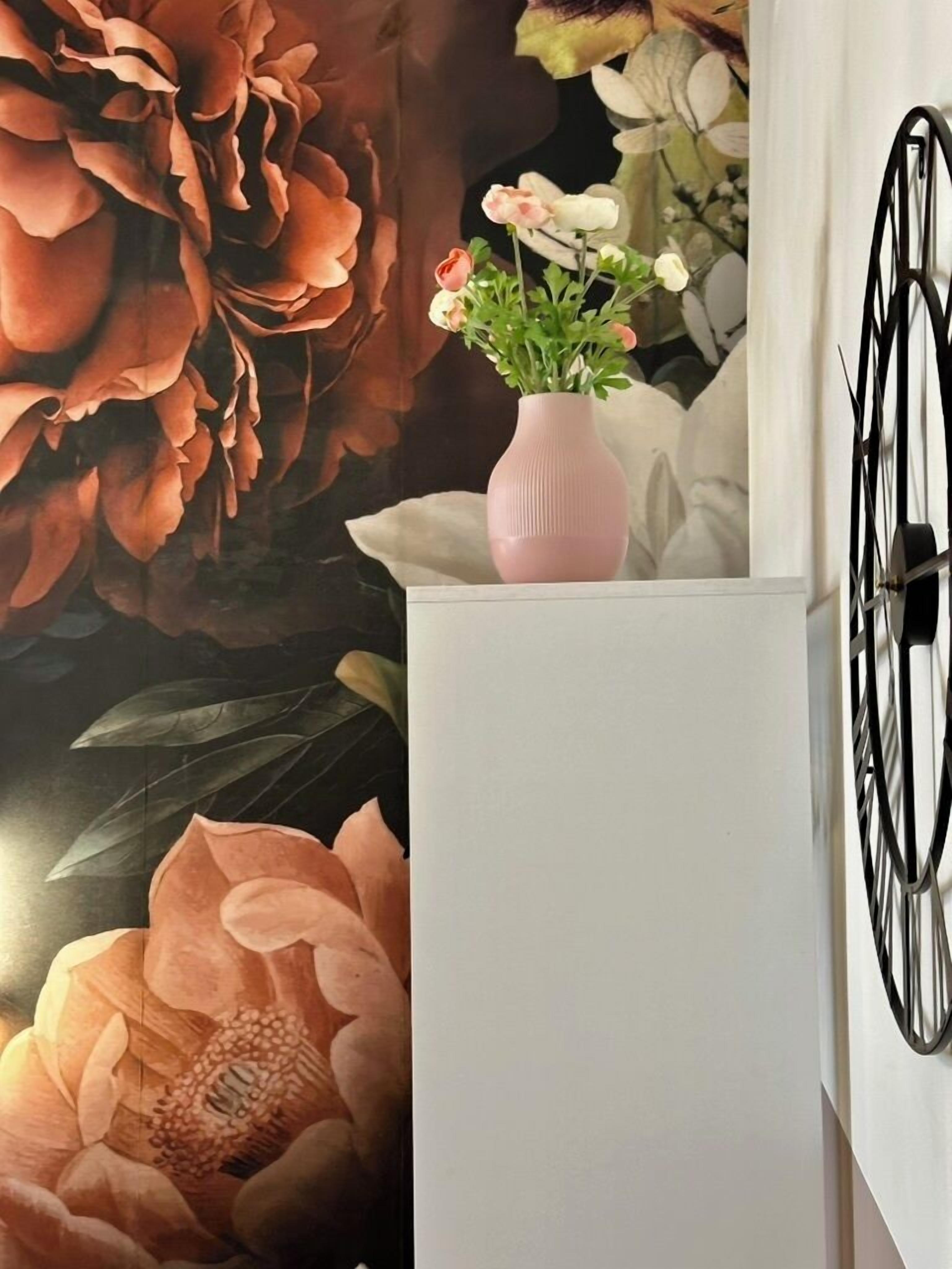 A room with a large floral mural, a white cabinet, and a pink vase with flowers.