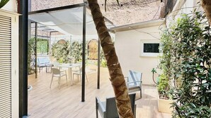 A covered outdoor patio with a table and chairs, surrounded by plants and a view of a building. - Vacanze Romane Suite 7 Languages (Rome)