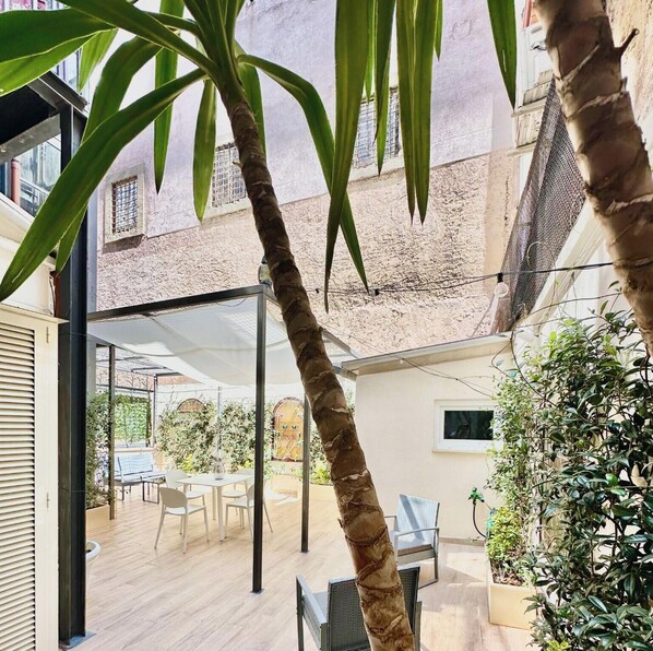 A covered outdoor patio with a table and chairs, surrounded by plants and a view of a building. - Vacanze Romane Suite 7 Languages (Rome)
