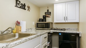 A compact kitchen with white cabinets, a stainless steel sink, a microwave, and a black refrigerator.