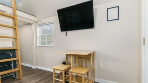 A room with a wooden ladder, two wooden stools, a TV mounted on the wall, and a window.