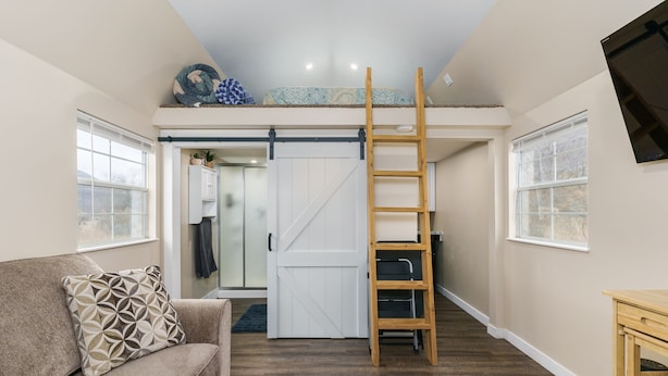 A loft bedroom with a bunk bed, a wooden ladder, a sliding door, and a view of the outdoors.
