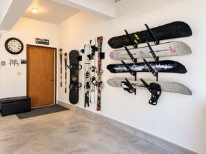 Un mur servant de rangement pour les skis, avec plusieurs paires de skis et de snowboards, une horloge et un panneau indiquant : « SKIS, POINTES VERS LE HAUT ».