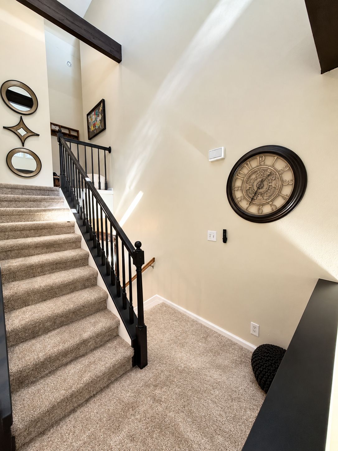 A carpeted staircase with a black handrail and a wall clock.