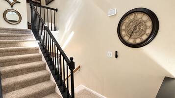A carpeted staircase with a black handrail and a wall clock.