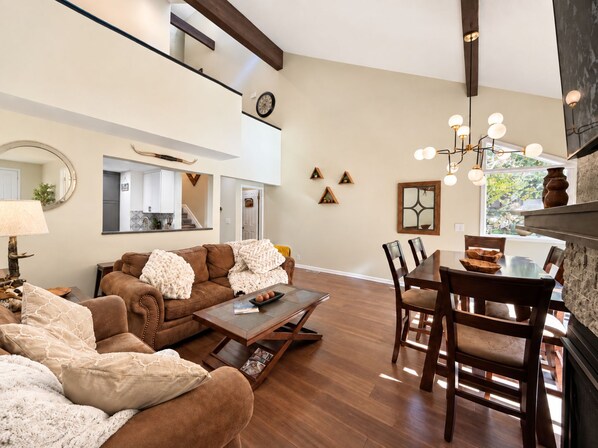 A spacious living room with a brown leather sofa, a coffee table, and a dining area with wooden chairs and a table.