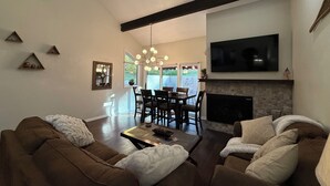 A living room with a fireplace, a dining area, and a TV mounted on the wall. - Cottonwood Chalet - New Remodel - Private Hot Tub 3BR/2BA + 4 Ski Resorts (Cottonwood Heights)