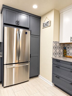 Eine moderne Küche mit einem Edelstahl-Kühlschrank, grauen Schränken und einem an der Wand befestigten Schild mit der Aufschrift 'EAT'.