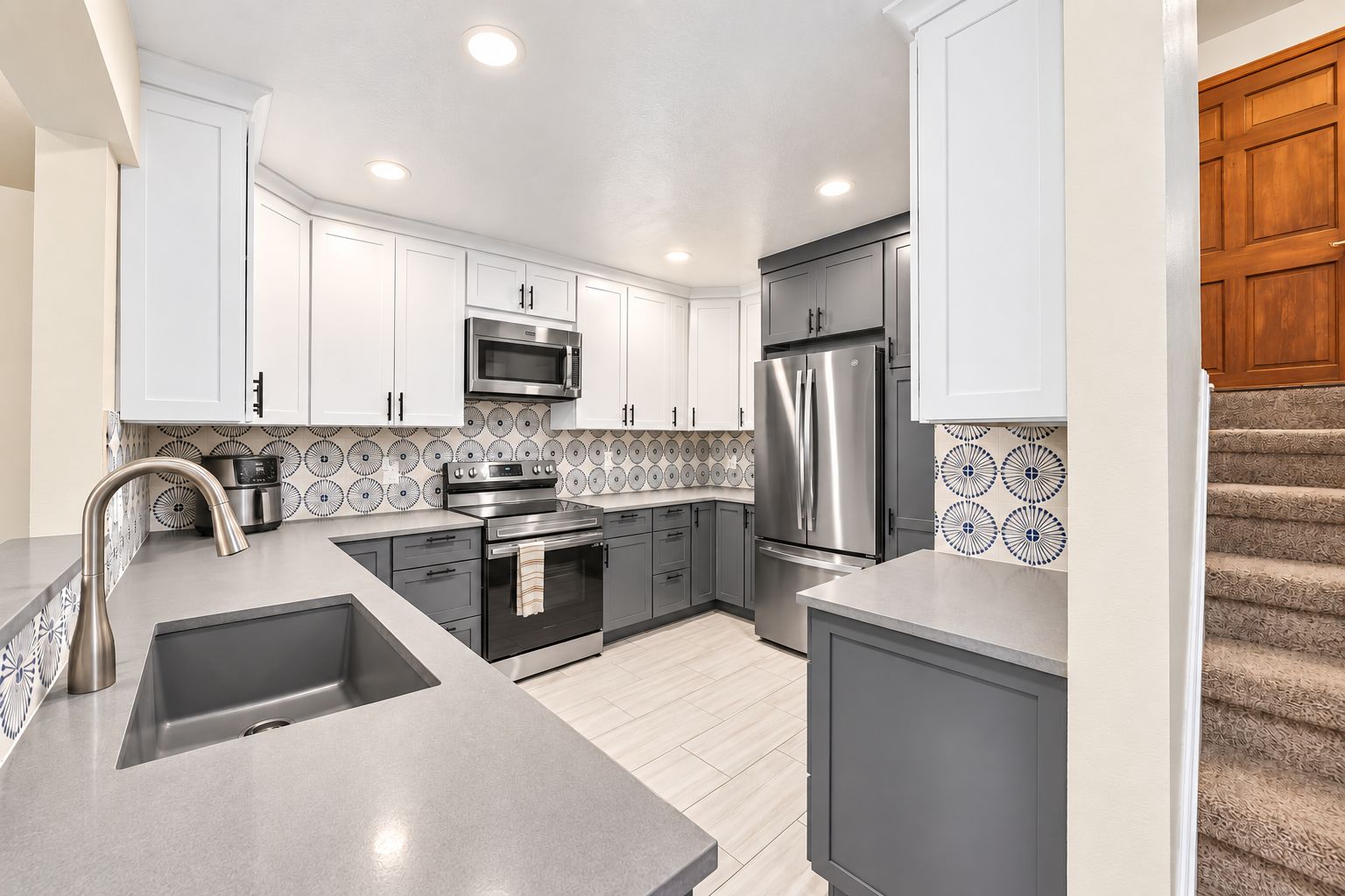 A modern kitchen with white cabinets, stainless steel appliances, and patterned backsplash tiles.