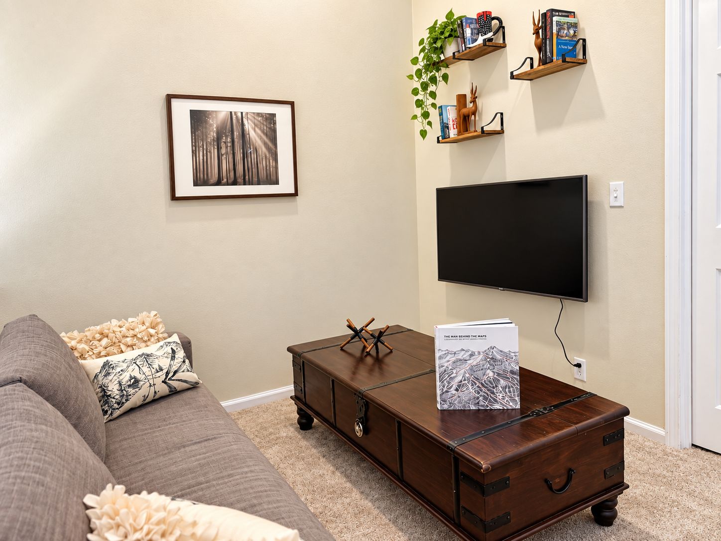 Ein Wohnzimmer mit braunem Sofa, einem Holztisch, einem gerahmten Bild, einem Flachbildfernseher und einem Bücherregal mit Büchern und Dekoration.