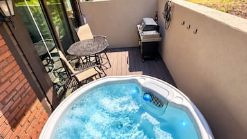 A hot tub on a patio with a table and chairs, surrounded by a brick wall and greenery.