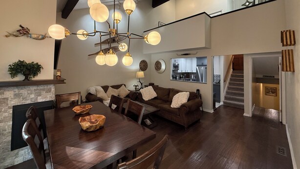 A spacious living area with a dining table, sofas, and a modern chandelier. A kitchen is visible in the background, and a staircase leads to an upper level. - Cottonwood Chalet - New Remodel - Private Hot Tub 3BR/2BA + 4 Ski Resorts (Cottonwood Heights)