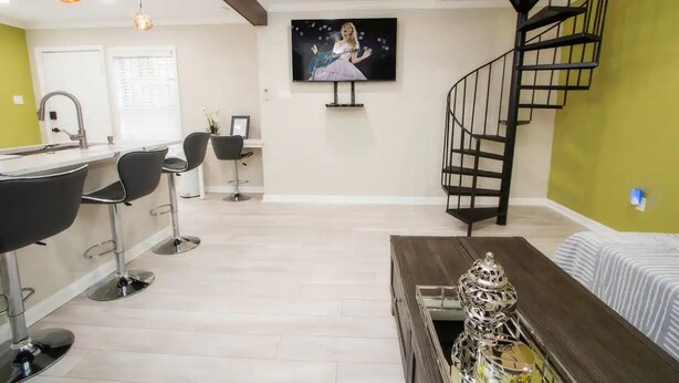 Una sala de estar moderna con televisor, una escalera y un comedor con taburetes de bar.