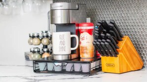 Una encimera de cocina con una cafetera, una taza, frascos de especias, un recipiente para café y un bloque de cuchillos.
