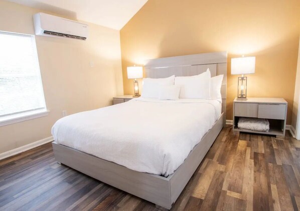 Una habitación de hotel con una cama grande, dos mesitas de noche con lámparas, un aire acondicionado de pared y una ventana con persianas.
