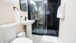 Un baño moderno con inodoro, lavamanos y zona de ducha con mampara de vidrio.