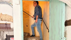 Una persona sale una scalinata di pietra con ringhiera, una porta con cornice verde e un cartello appeso al muro.