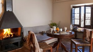 A cozy room with a fireplace, a sofa, a round table with a vase and books, and a window with open shutters. - L'Escala-Ventalló. Cosy, WiFi & Rooftop terrace EG (Ventalló)
