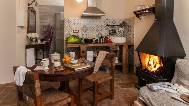 A cozy living room with a fireplace, a dining area with a table and chairs, and a kitchen with a sink and stove. - L'Escala-Ventalló. Cosy, WiFi & Rooftop terrace EG (Ventalló)