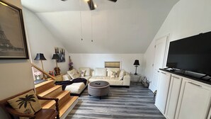 Un salon avec un canapé, un pouf et un téléviseur posé sur un meuble.