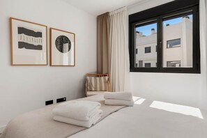 Una habitació d'hotel moderna amb un llit, dues obres d'art emmarcades, una finestra amb cortines i vista a edificis a l'exterior.
