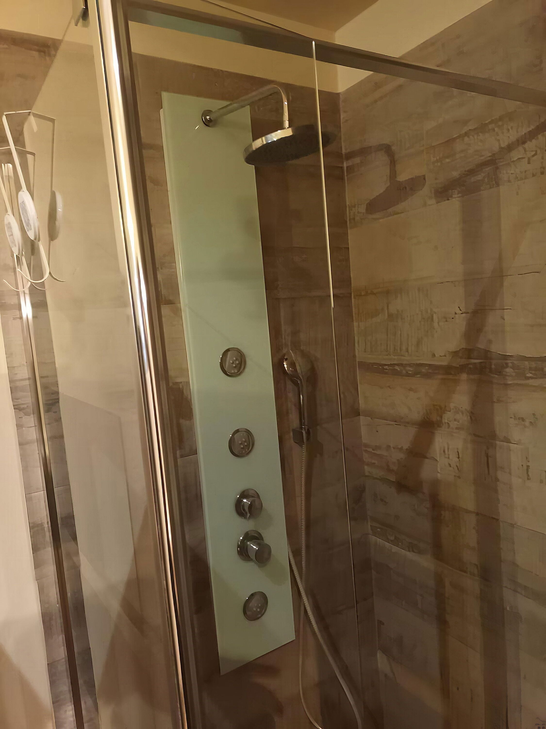 Doccia vetrata con pannello di controllo, soffione a mano e rubinetto a parete.
