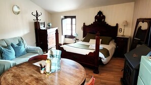 Un dormitorio con cama con dosel, un aparador de madera, una mesa redonda con sillas y una pequeña cocina con estufa.