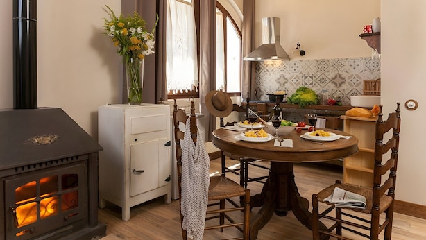 Una cocina acogedora con una estufa de leña, una mesa de comedor con sillas y un ventanal con cortinas.