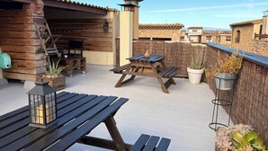 En tagterrasse med træbænke, et bord, plantekrukker og en stenvæg.