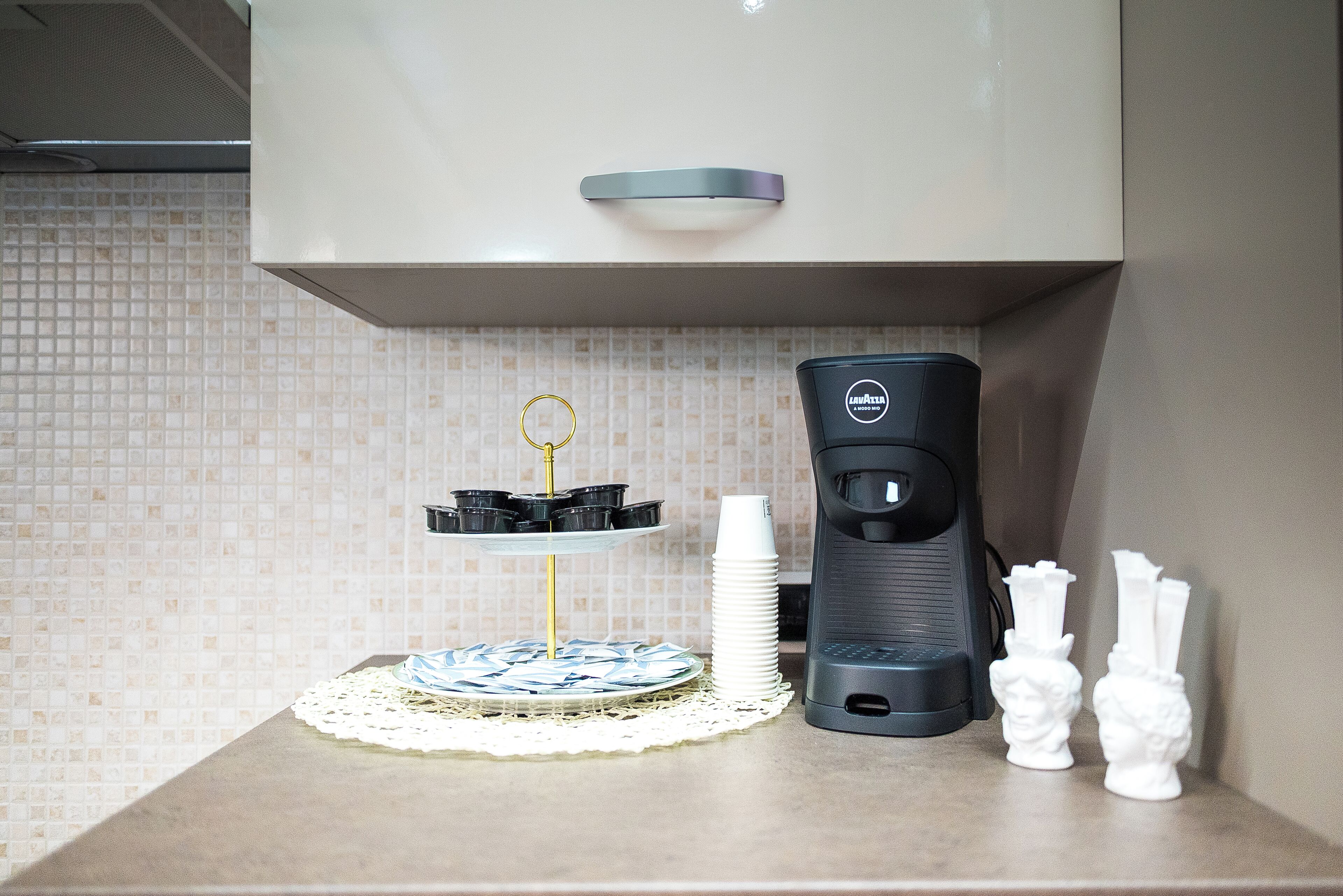 A kitchen counter with a coffee maker, a doily, a plate with a cake, and two small white vases.