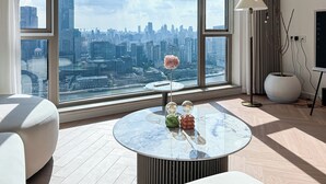 Un salón moderno con un ventanal amplio que ofrece vistas a la ciudad, una mesa de centro redonda de cristal con adornos y una decoración de estilo minimalista.